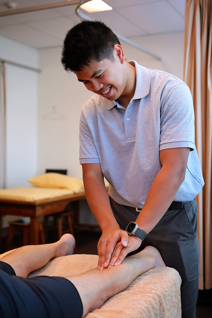 Physiotherapist smiling while performing a leg massage on a patient lying on a treatment table.